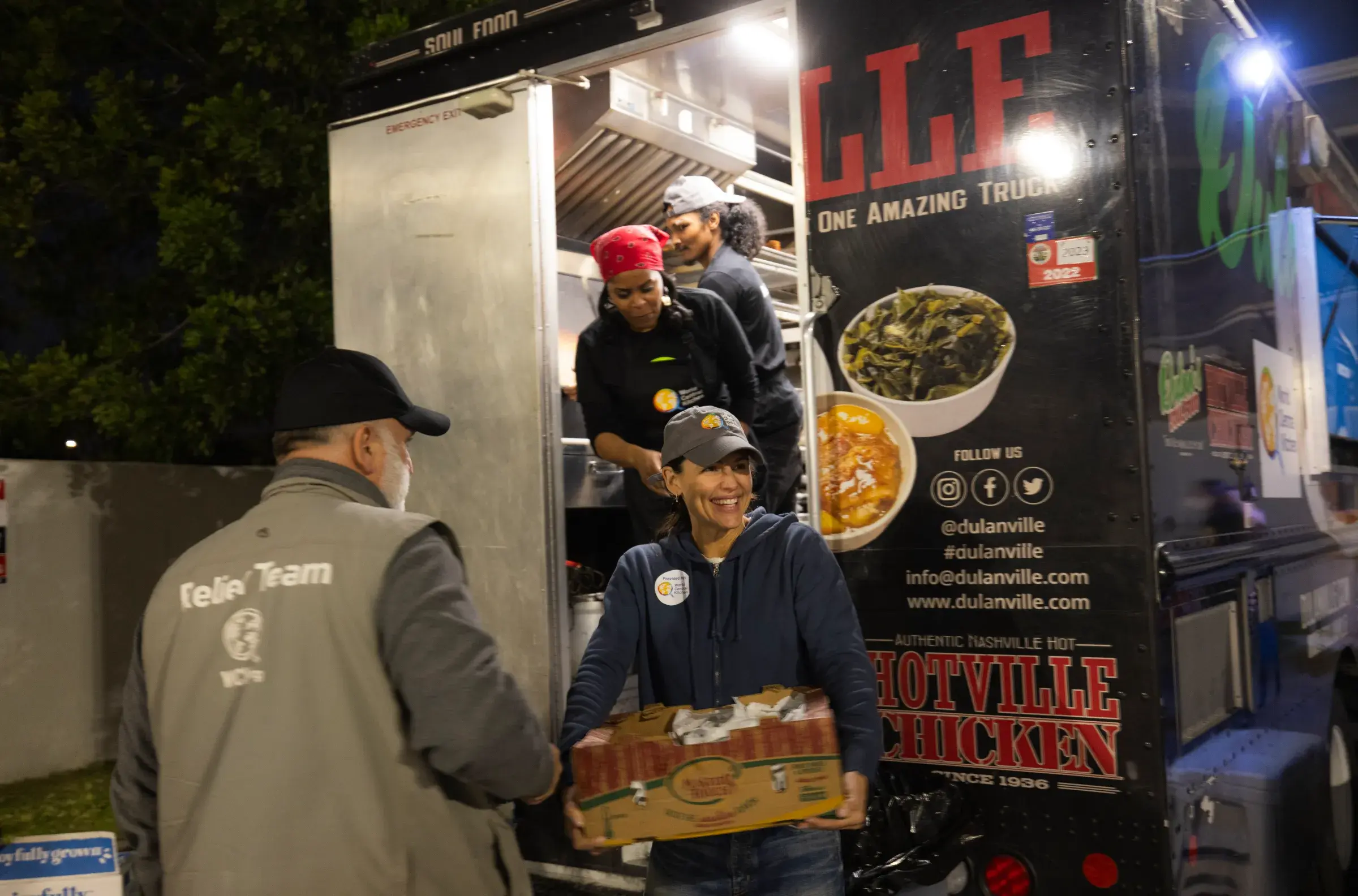 An image of José Andrés, Kim Prince, and others serving good from the back of the Hotville Chicken food truck